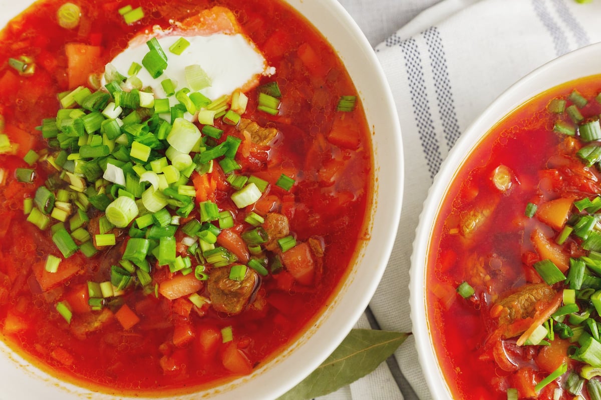 Two bowls of vibrant red vegetable soup garnished with fresh herbs