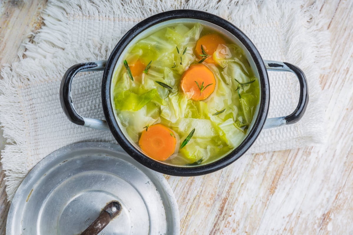 A pot of fresh cabbage soup on a white wooden table
